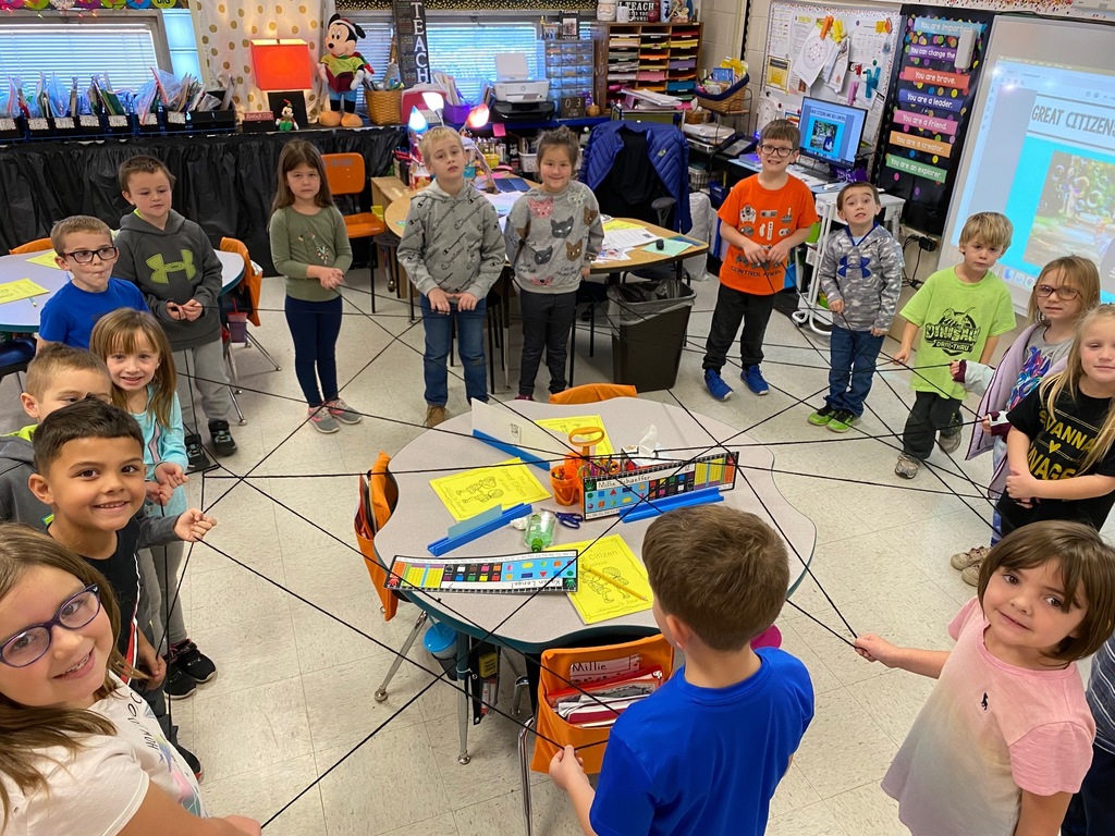 Group of 1st grade students stand in a circle holding part of a large piece of string to create a giant web.