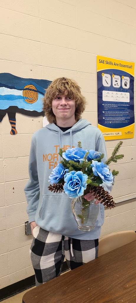 high school students holds an arrangement of pint and blue silk flowers 