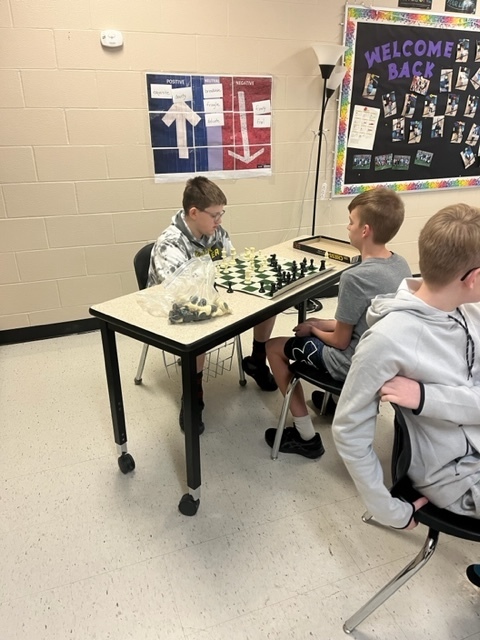 two students sit across the table and  play chess 
