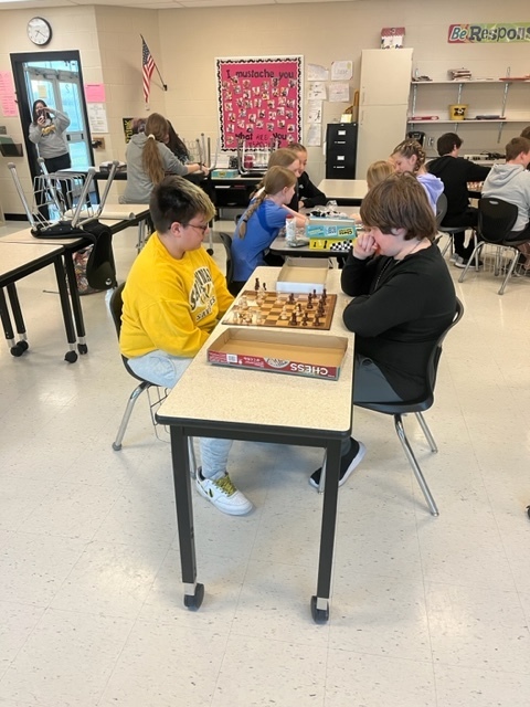 two students play chess while 5 others sit in the background